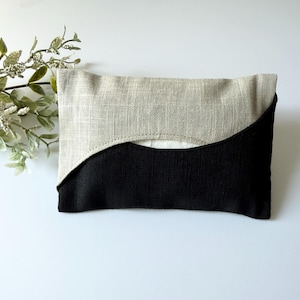 May include: A rectangular fabric pouch featuring a two-tone design with a beige linen-textured upper section and a solid black lower section. The two colours meet in a curved, wave-like seam across the front, revealing a white interior lining.