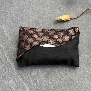 May include: A rectangular fabric pouch featuring a solid black lower section and an upper section made of black mesh overlay with a copper-coloured floral pattern. The pouch has a small opening at the top centre, revealing a white interior lining.
