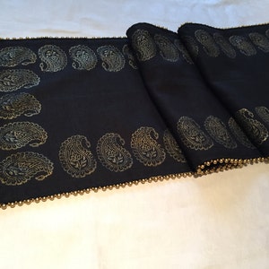 May include: Black table runner with a gold paisley pattern and a gold beaded trim.