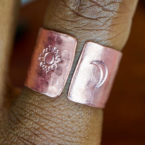 May include: A copper ring with a sun and moon design. The ring is worn on a finger.