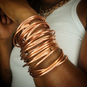 Puede incluir: Un brazalete de cobre hecho de m&uacute;ltiples bandas finas entrelazadas. El brazalete se lleva en la mu&ntilde;eca y es una pieza de joyer&iacute;a llamativa.