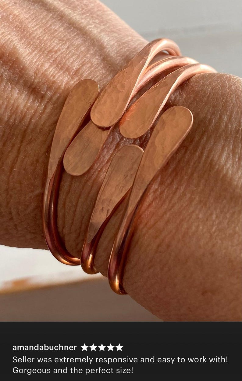 Puede incluir: Un conjunto de tres pulseras de cobre con acabado martillado. Las pulseras est&aacute;n apiladas una encima de la otra y tienen una forma redondeada.