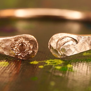 May include: A hammered copper ring with a sun and moon design. The ring is open and has a textured finish.