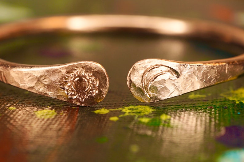 May include: A hammered copper ring with a sun and moon design. The ring is open and has a textured finish.