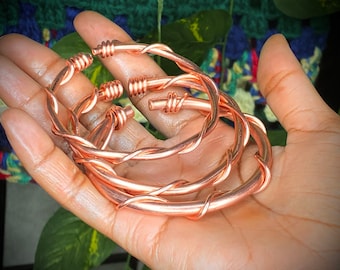 May include: Three copper wire bracelets with a twisted design. The bracelets are stacked on top of each other.