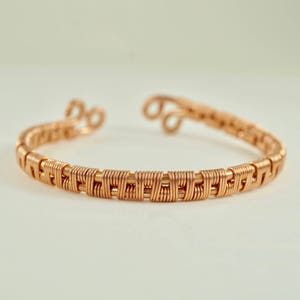 Puede incluir: Un brazalete de alambre envuelto en oro rosa con un diseño tejido.