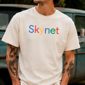 Può includere: Una t-shirt a maniche corte color crema con la parola Skynet stampata sul petto. Le lettere sono colorate in blu, rosso, giallo, blu, verde e rosso, imitando uno stile grafico multicolore sulla parte anteriore del capo.