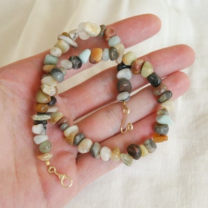 May include: A necklace made of various coloured stones, including brown, white, grey, and green. The stones are strung together on a gold chain.