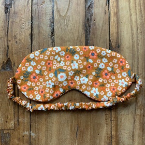 May include: An eye mask with a floral pattern in shades of orange, white, and blue. The mask has an elastic band for a comfortable fit. The sleep mask is designed to block out light for better sleep.