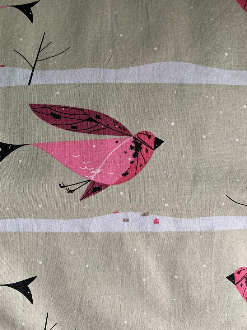 May include: Fabric with a repeating pattern of stylized pink birds in flight against a winter landscape. The birds have dark accents and are set against a neutral background with white snow and small houses.