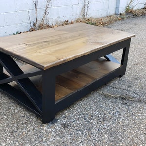 May include: A wooden coffee table with a black painted frame and a geometric design. The table has a lower shelf and a natural wood top.