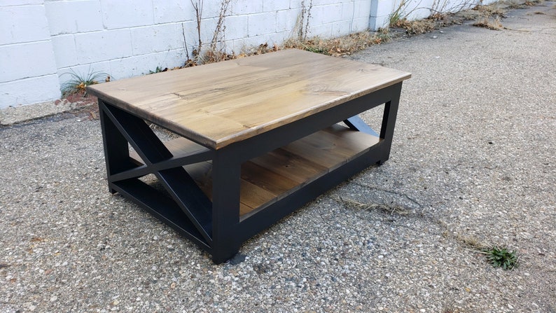 May include: A wooden coffee table with a black painted frame and a geometric design. The table has a lower shelf and a natural wood top.