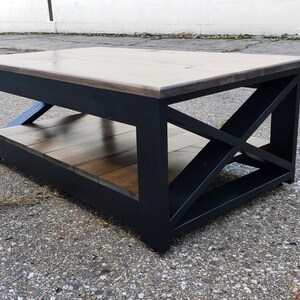 May include: A black coffee table with a wood top and a lower shelf. The table has a unique X-shaped design on the legs.