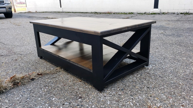 May include: A black coffee table with a wood top and a lower shelf. The table has a unique X-shaped design on the legs.