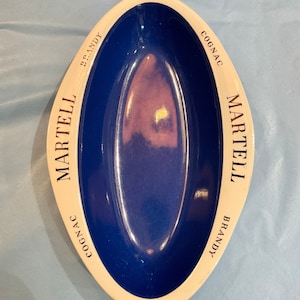 Könnte beinhalten: Ovale Martell Brandy-Schale mit blauem Innenraum und cremefarbenem Rand. Die Schale hat das Martell-Logo und die Worte "Cognac" und "Brandy" in Schwarz. Ein Vintage-Artikel.