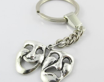 May include: Silver-toned keychain featuring two theatrical masks, one smiling and one frowning, connected by a chain to a key ring. The masks are detailed with facial features. The keychain is a decorative accessory.