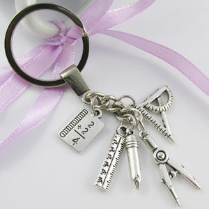 May include: Silver keychain with a purple ribbon. The keychain has charms of a ruler, protractor, compass, and a notebook with the text "4/2N" on it.