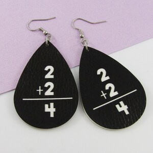 May include: A pair of black leather teardrop earrings with white text that reads "2 + 2 / 4".