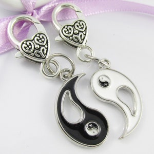 May include: Two silver-tone heart-shaped clasps with a black and white yin yang charm. The yin yang charm is made of metal and has a black and white enamel finish.