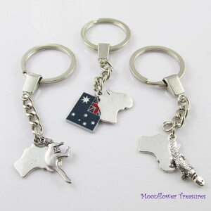 May include: Three silver keychains with charms. One keychain has a kangaroo charm, another has an Australian flag charm, and the third has an alligator charm. The charms are attached to a chain and a silver key ring.
