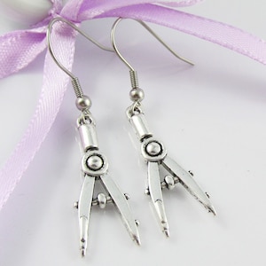 May include: A pair of silver compass earrings. The earrings are hanging from silver hooks.