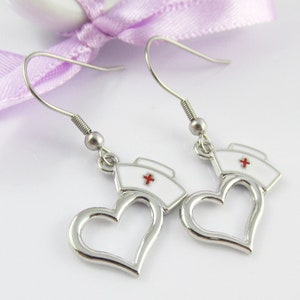 May include: A pair of silver earrings with a white heart and a red cross on top. The heart is open and the cross is on a white nurse's cap.