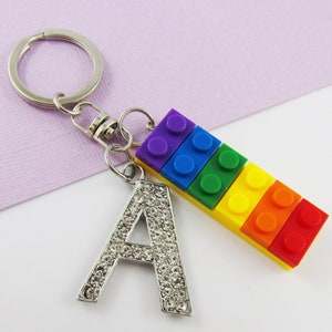 May include: A silver keyring with a rainbow-coloured Lego brick charm and a silver letter A charm covered in rhinestones.