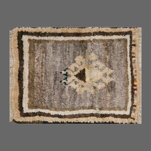 May include: A brown and beige rug with a geometric pattern in the centre. The rug has a fringed border.