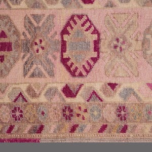 May include: Close-up of a pink and beige patterned rug. The rug features geometric shapes in shades of pink, gray, and burgundy. The design includes diamond, octagonal, and floral motifs.