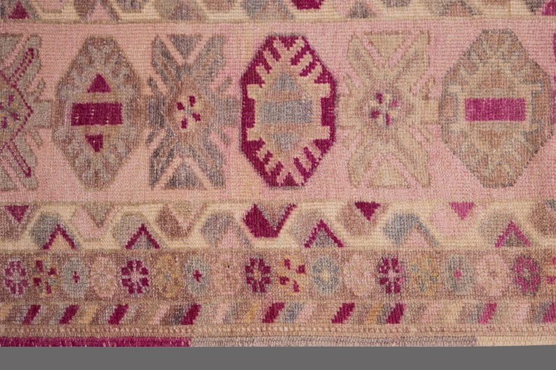 May include: Close-up of a pink and beige patterned rug. The rug features geometric shapes in shades of pink, gray, and burgundy. The design includes diamond, octagonal, and floral motifs.