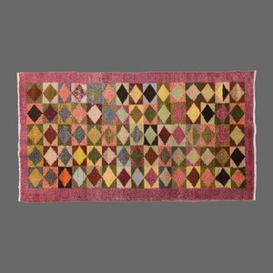 Può includere: Tappeto rettangolare con un motivo a rombi ripetuto in vari colori, tra cui rosa, verde, giallo e marrone. Il tappeto ha un bordo rosa e un aspetto strutturato, adatto per l'arredamento della casa.