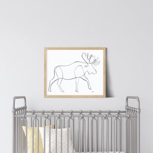 May include: A white crib with a yellow and white patterned pillow and a wooden rocking horse. A framed black and white line drawing of a moose is hanging on the wall above the crib.