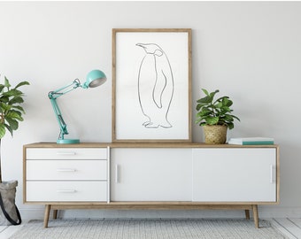以下が含まれることがあります： ペンギンのミニマリストラインアートプリントの額入り。アートワークは、白と木目調のキャビネットに、ターコイズのデスクランプと鉢植えの植物と一緒に展示されています。キャビネットには3つの引き出しと引き戸があります。