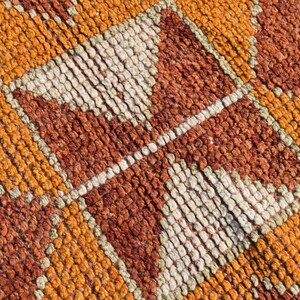 K&ouml;nnte beinhalten: Nahaufnahme eines gewebten Teppichs mit einem geometrischen Muster in Orange-, Braun- und Wei&szlig;t&ouml;nen.