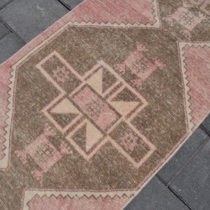 May include: A pink and brown vintage rug with a geometric pattern. The rug has a faded, distressed look and is perfect for adding a touch of bohemian style to any room.