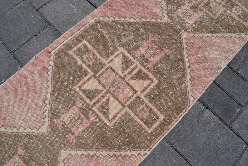 May include: A pink and brown vintage rug with a geometric pattern. The rug has a faded, distressed look and is perfect for adding a touch of bohemian style to any room.