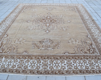 Puede incluir: Una alfombra beige con un patrón floral marrón. La alfombra tiene un gran medallón central y un borde con un diseño repetitivo.
