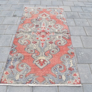 May include: A vintage red and gray patterned rug with a floral design. The rug has a fringed edge and is made of wool.