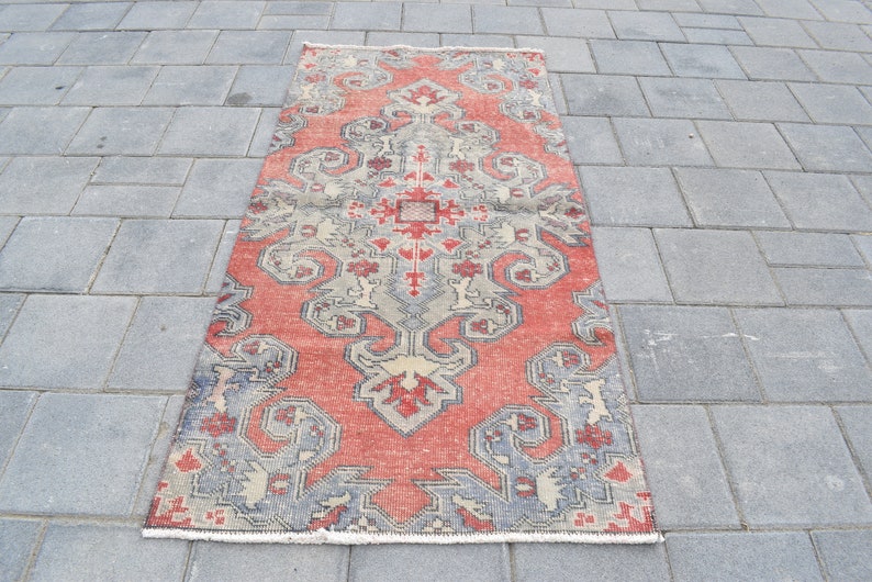 May include: A vintage red and gray patterned rug with a floral design. The rug has a fringed edge and is made of wool.