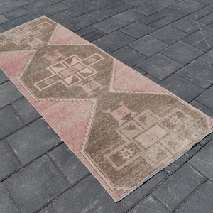 May include: A pink and brown patterned runner rug with a geometric design. The rug is made of a soft, woven material and has a distressed look.