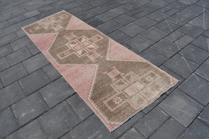 May include: A pink and brown patterned runner rug with a geometric design. The rug is made of a soft, woven material and has a distressed look.