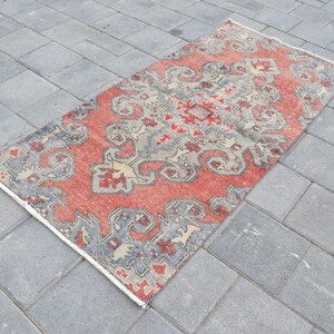 May include: A red, gray, and cream patterned rug with a geometric design. The rug is laid out on a gray concrete surface.