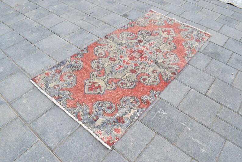May include: A red, gray, and cream patterned rug with a geometric design. The rug is laid out on a gray concrete surface.