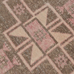 May include: A close-up of a brown and pink patterned rug with a geometric design. The rug has a worn and faded look, giving it a vintage feel.