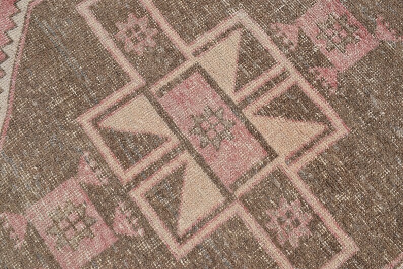 May include: A close-up of a brown and pink patterned rug with a geometric design. The rug has a worn and faded look, giving it a vintage feel.