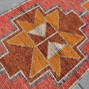 K&ouml;nnte beinhalten: Nahaufnahme eines roten, orangefarbenen und braunen Teppichs mit geometrischem Muster. Der Teppich hat einen Fransenrand und ist aus gewebten Fasern gefertigt.