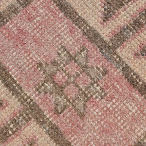 May include: Close-up of a woven rug with a geometric pattern in shades of pink, brown, and beige.