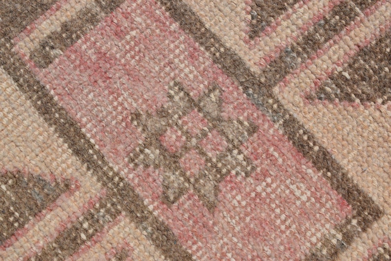 May include: Close-up of a woven rug with a geometric pattern in shades of pink, brown, and beige.
