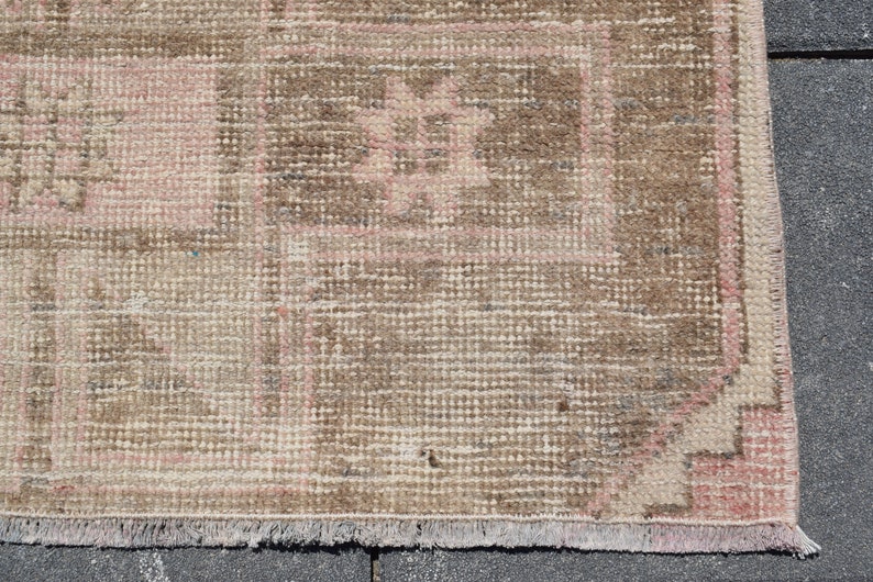 May include: A vintage rug with a brown and pink geometric pattern. The rug has a fringe border and is made of a woven material.