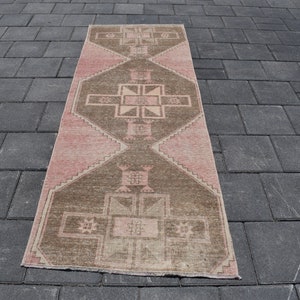 May include: A long, rectangular rug with a pink and brown geometric pattern. The rug has a distressed, vintage look.